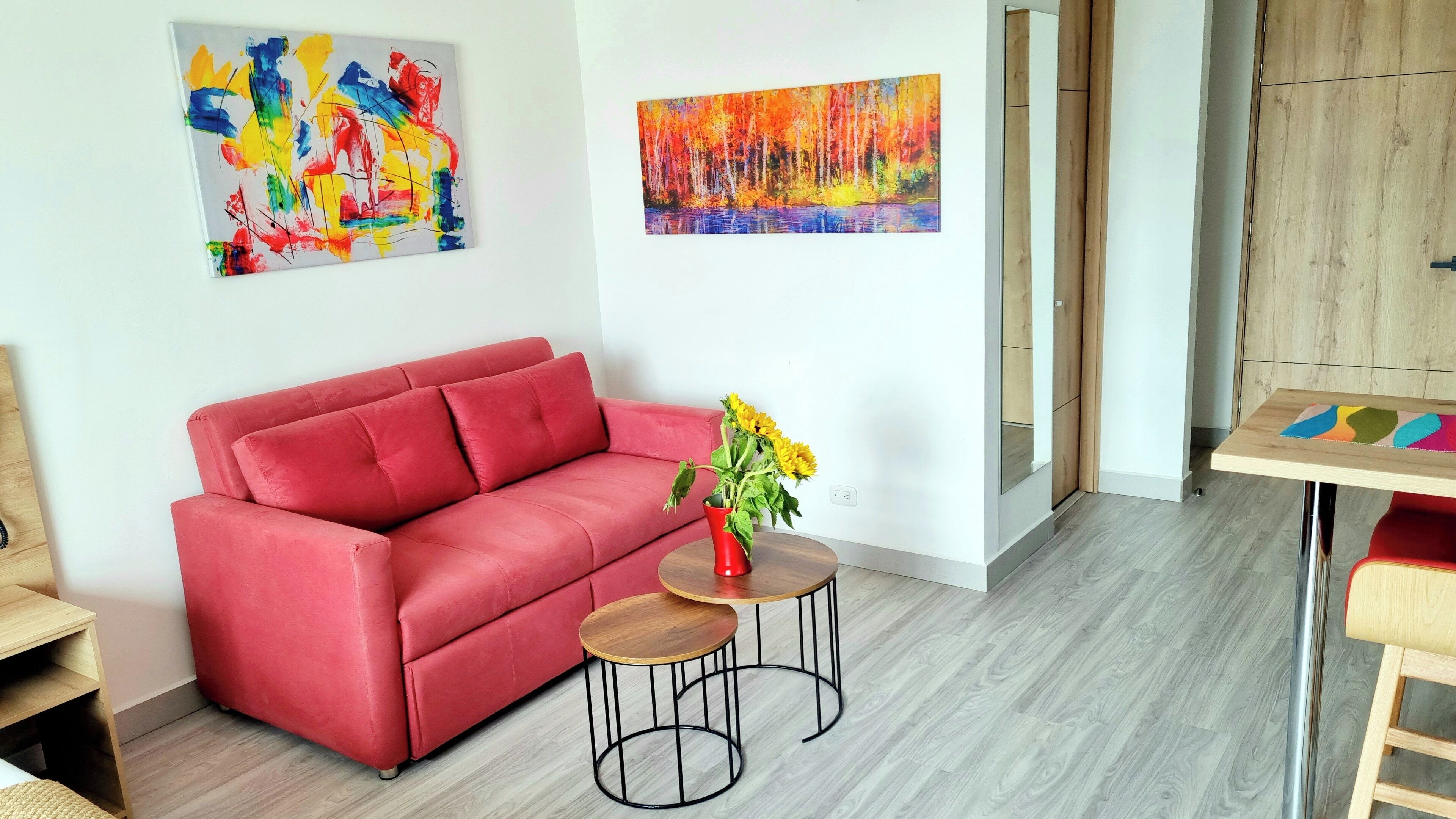 A red sofa, two small round tables with metal legs, and a vase with sunflowers.