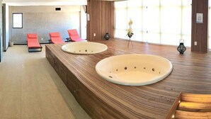 A modern bathroom with two large sinks, a wooden vanity, and a seating area with red chairs. - Vacanze - Time (Maceió)