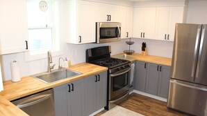 Uma cozinha moderna com armários brancos, uma geladeira de aço inoxidável, micro-ondas, fogão e lava-louças.