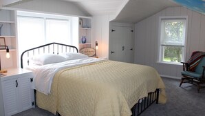 Quarto com cama, cômoda, cadeira e janela.