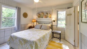 A bedroom with a bed, a ceiling fan, a nightstand with a lamp, a painting on the wall, and a door. - Riverfront Florida Escape w/ Grill & Fire Pit! (Tallahassee)