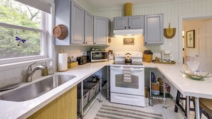 A kitchen with white cabinets, a microwave, an oven, a sink, and a window with a view of trees. - Riverfront Florida Escape w/ Grill & Fire Pit! (Tallahassee)