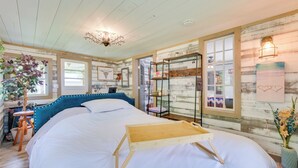 Ein gemütliches Zimmer mit einem großen Bett, einem Holfnachtkästchen, einer hängenden Pflanze und einer rustikalen Wand mit Kunstwerken.