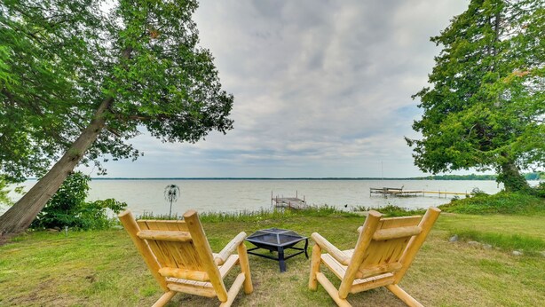 Zwei hölzerne Adirondack-Stühle, die auf einen See mit einem Steg und einem Pavillon im Hintergrund zeigen.