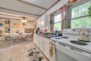 A kitchen with white cabinets, a stove, and a dining area with chairs.