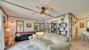 Ein gemütliches Wohnzimmer mit grauem Sofa, Deckenventilator und Bücherregal voller Bücher und Dekoration.