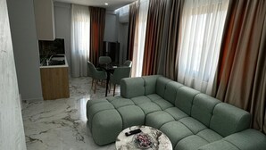 A modern living room with a sectional sofa, a marble coffee table, and a dining area with chairs. - Albania Dream Holidays Accommodation (Sarandë)