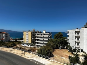 A coastal residential area with multi-story buildings, a road, and a clear view of the sea. - Albania Dream Holidays Accommodation (Sarandë)