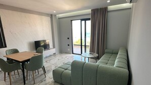 A modern living room with a marble floor, a green sofa, a dining table with chairs, and a TV. - Albania Dream Holidays Accommodation (Sarandë)