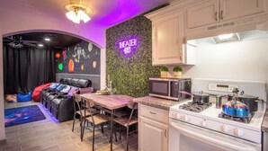 Un espace de vie compact comprenant un coin cuisine, un coin repas, un canapé et un mur orné d'un néon.