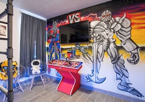 Ein Zimmer mit einer großen Wandmalerei, einem Flachbildfernseher, einem Kicker und einem kleinen Tisch mit Spielzeug.