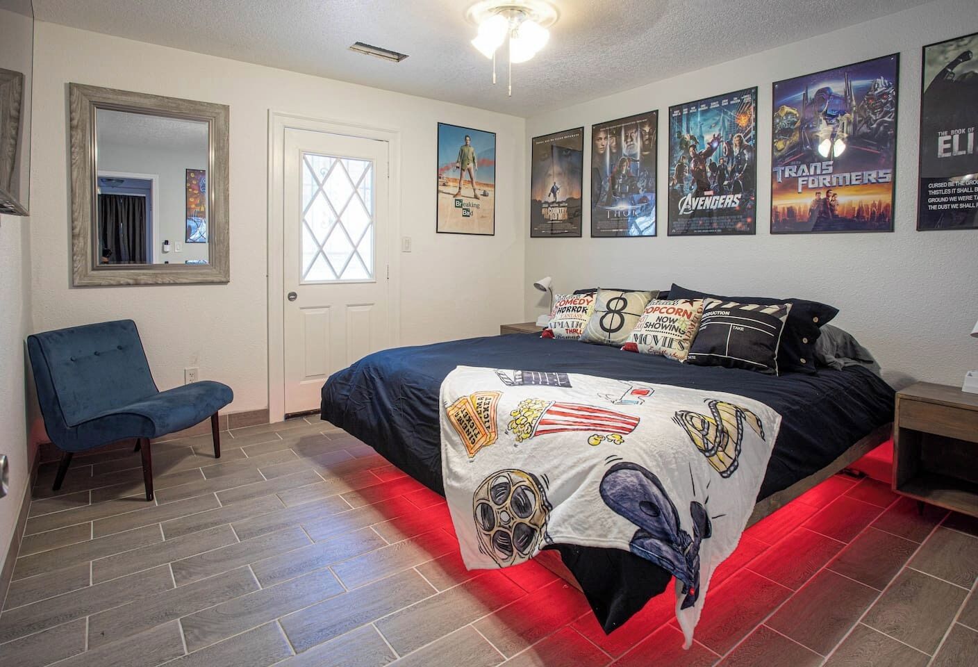Un dormitorio con cama, carteles en la pared, una silla y una puerta.