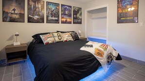 Une chambre à coucher avec un lit, des affiches sur les murs, une table de chevet et une lampe.