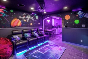 Ein Zimmer mit einer Couch, einem roten Sitzsack, einem Deckenventilator, einer Küchenzeile und einer Wand mit Weltraumdekorationen.