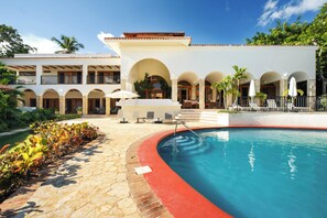 A pool area with a red border, lounge chairs, and a building with multiple balconies and arches. - Stunning Ocean View Villa (La Romana)