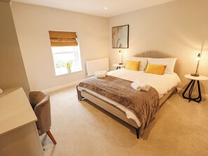 A bedroom with a bed, bedside tables, a chair, a window with blinds, and a radiator.