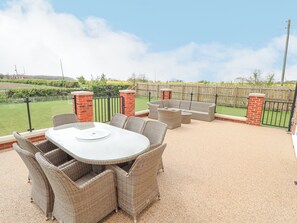 An outdoor patio with wicker furniture, a table, and a view of a grassy area beyond a wooden fence.