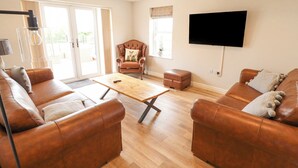 Un salón amplio con sofás de cuero, una mesa de centro de madera y un televisor instalado en la pared.