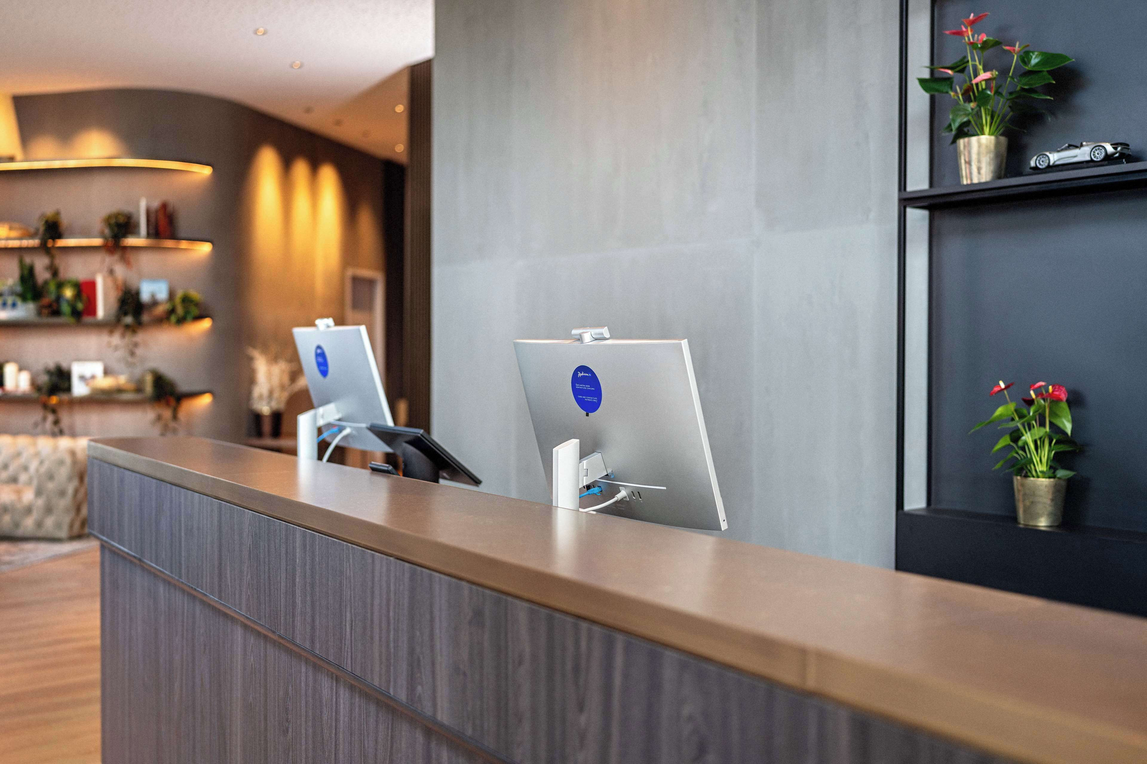 Ein moderner Empfangstresen mit einem Laptop, einem Telefon und einem Schild, das einen Self-Service-Check-in weist.