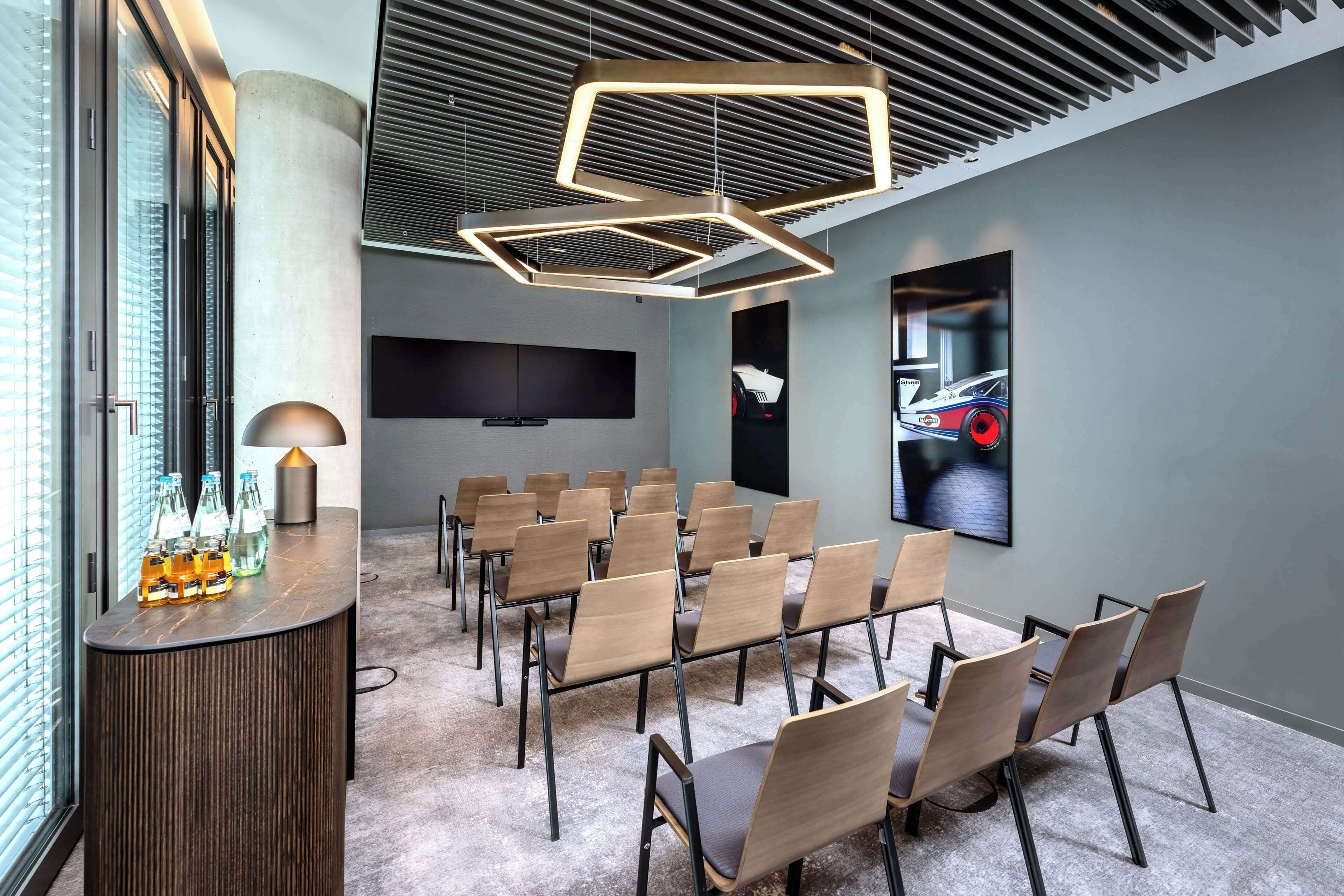 Ett konferensrum med modern design, inrett med ett långt bord och stolar, en stor skärm och en unik, geometrisk formgiven lampa.