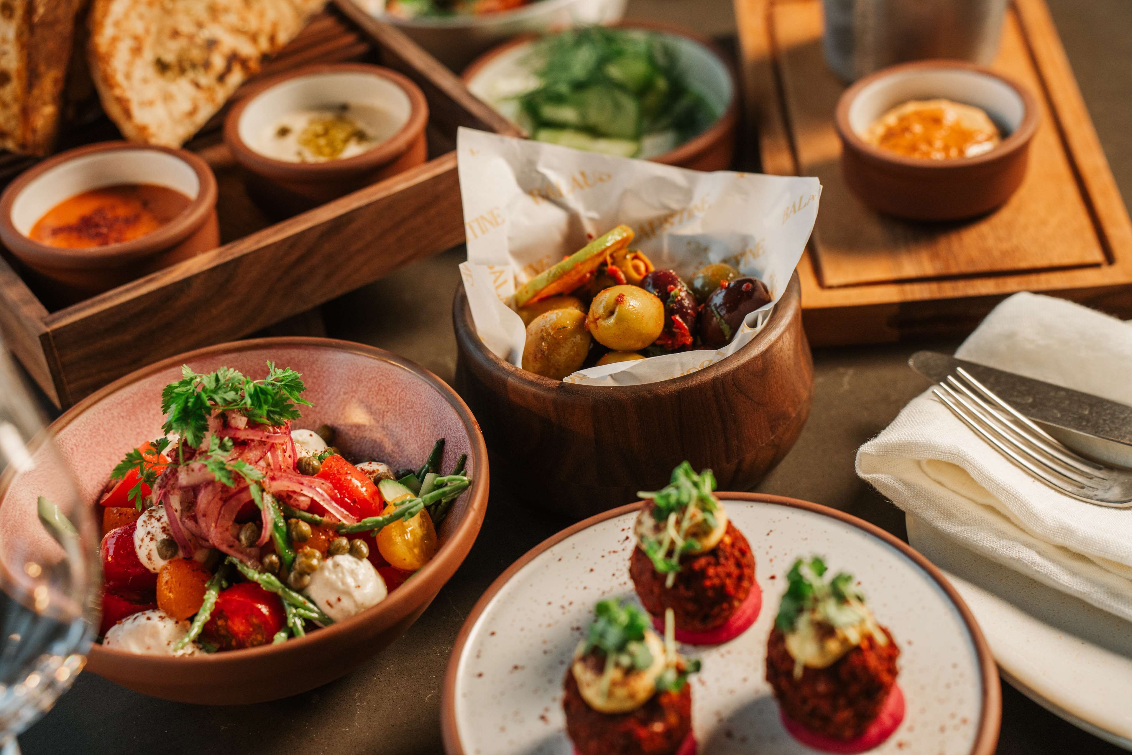 Variedad de platos sobre una mesa de madera, incluyendo un tazón de ensalada, un plato de aperitivos y varios recipientes pequeños con salsas.