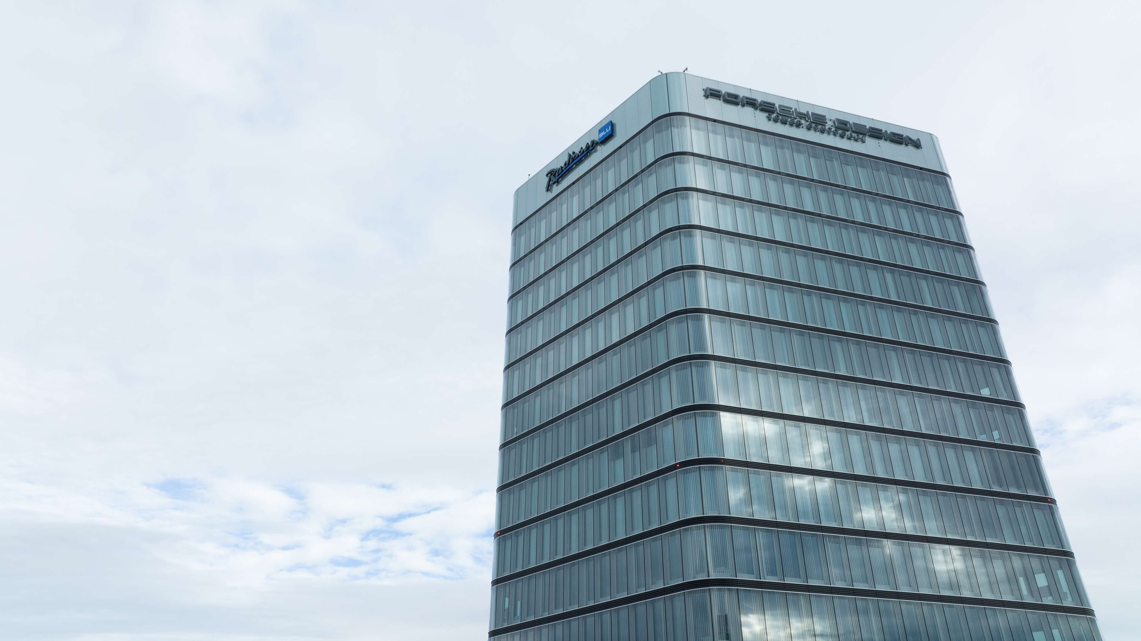 A tall, modern building with a glass facade and the Porsche Design logo at the top.