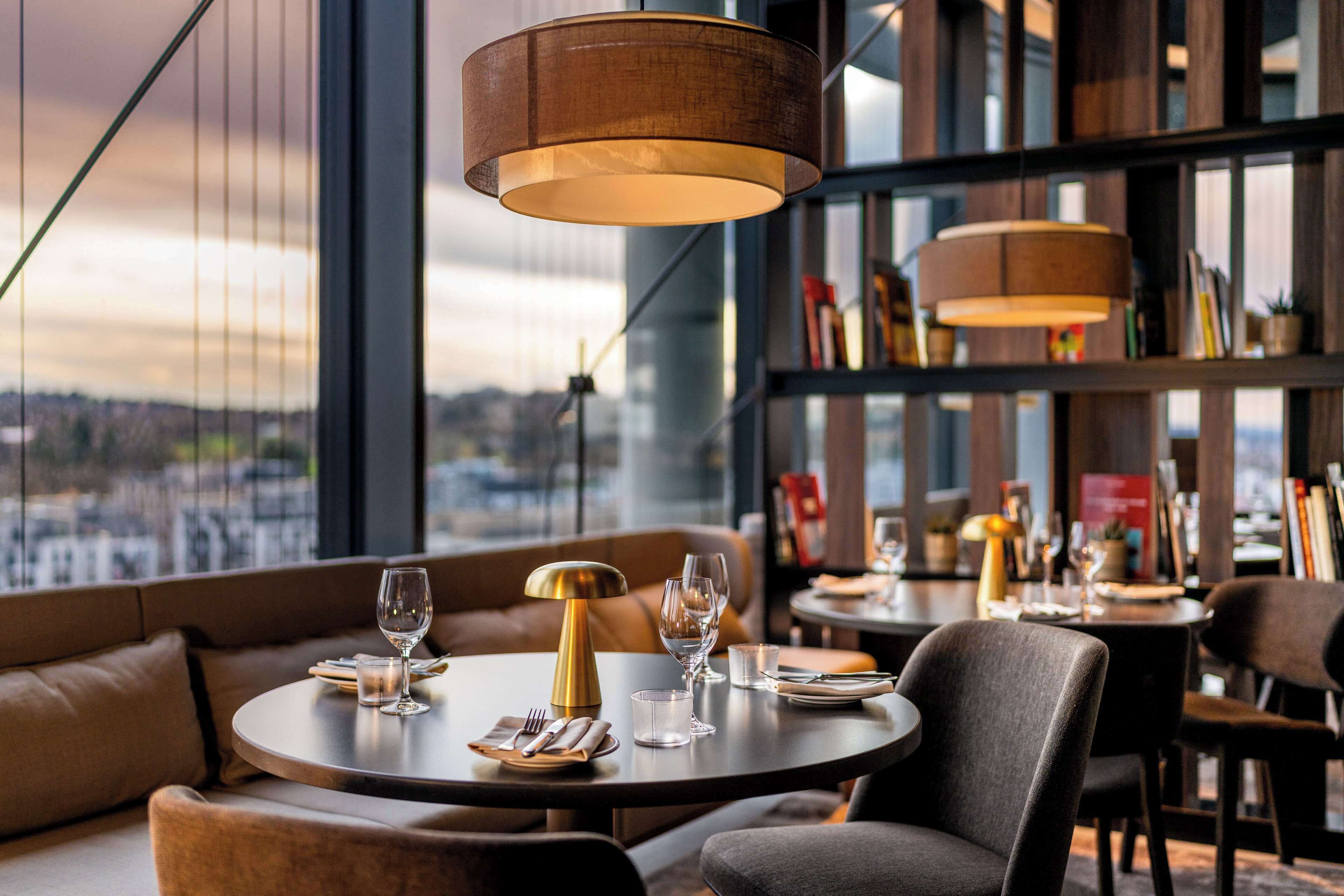Ein Restaurant mit runden Tischen, Ledersitzgelegenheiten und Pendelleuchten.