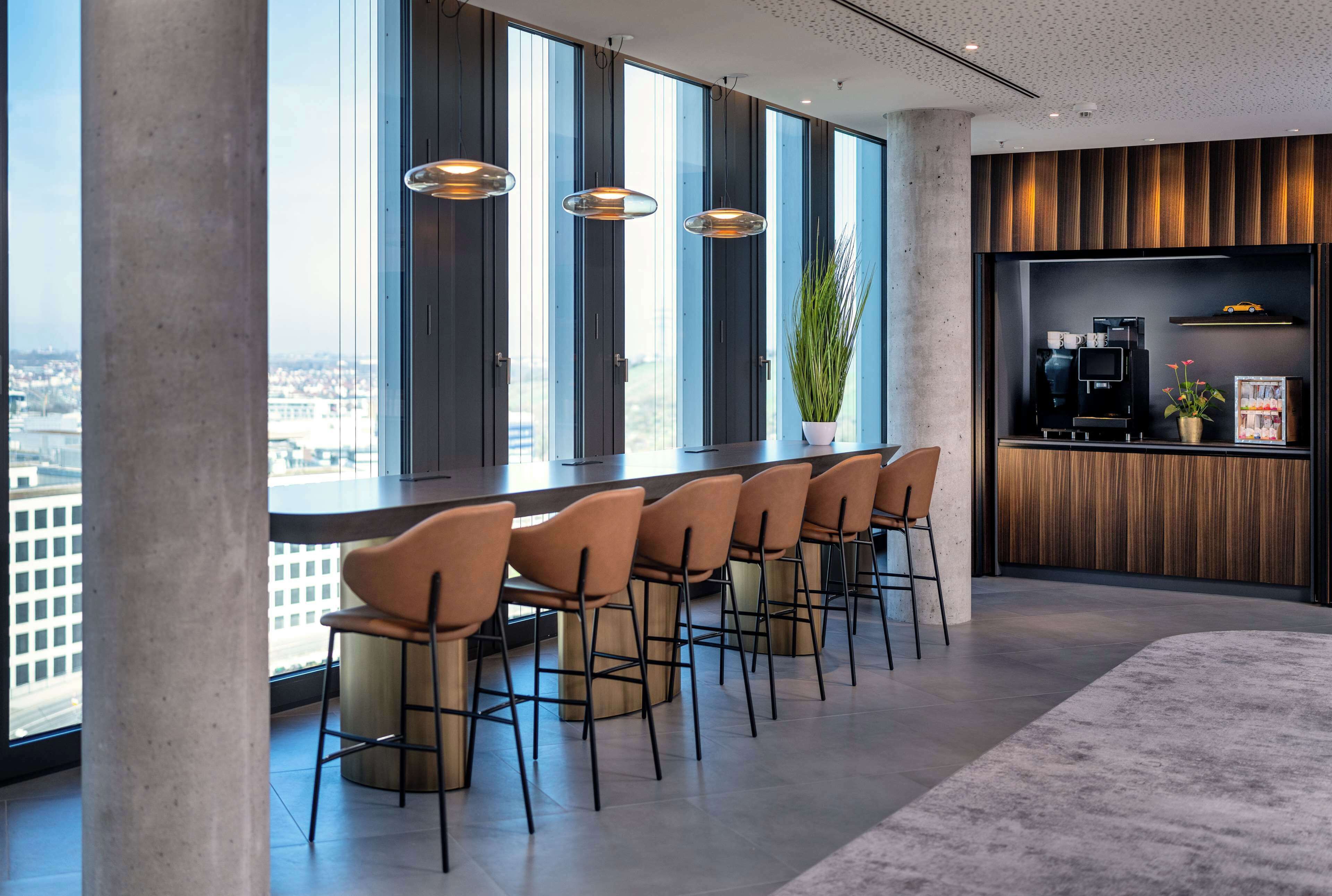 Et moderne barområde med en lang disk, flere barstole og en kaffemaskine.