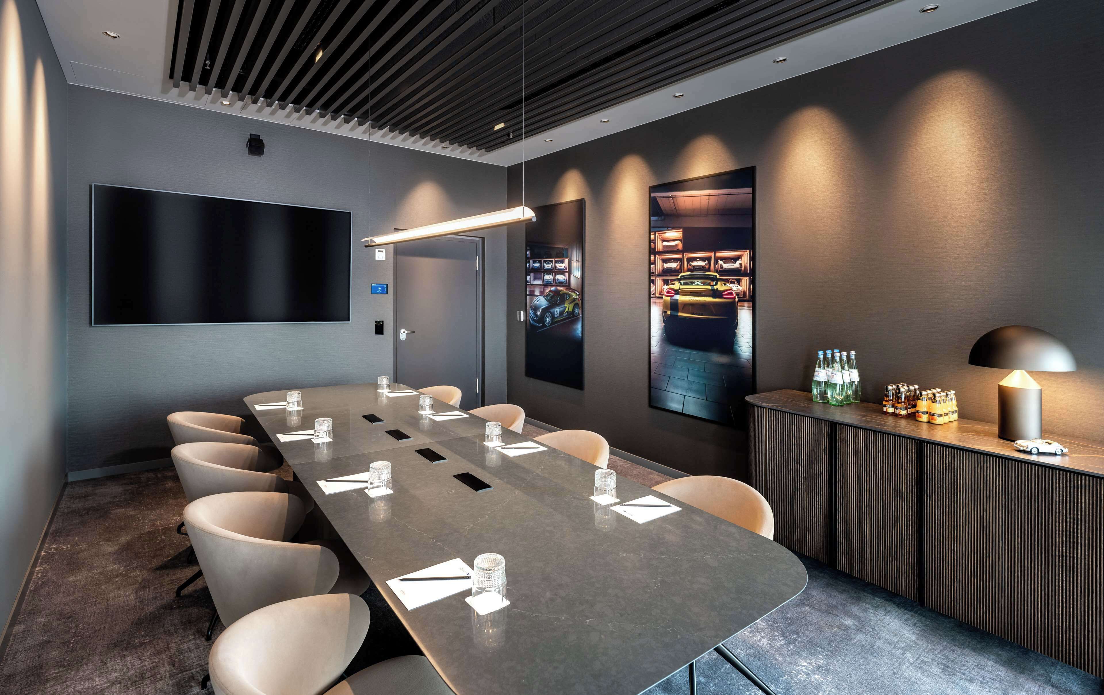 Una sala de conferencias con una larga mesa, sillas, un televisor de pantalla plana, un mostrador de recepción con botellas y una obra de arte colgada en la pared.