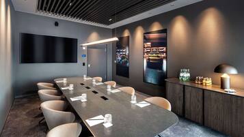 Una sala de conferencias con una larga mesa, sillas, un televisor de pantalla plana, un mostrador de recepción con botellas y una obra de arte colgada en la pared.