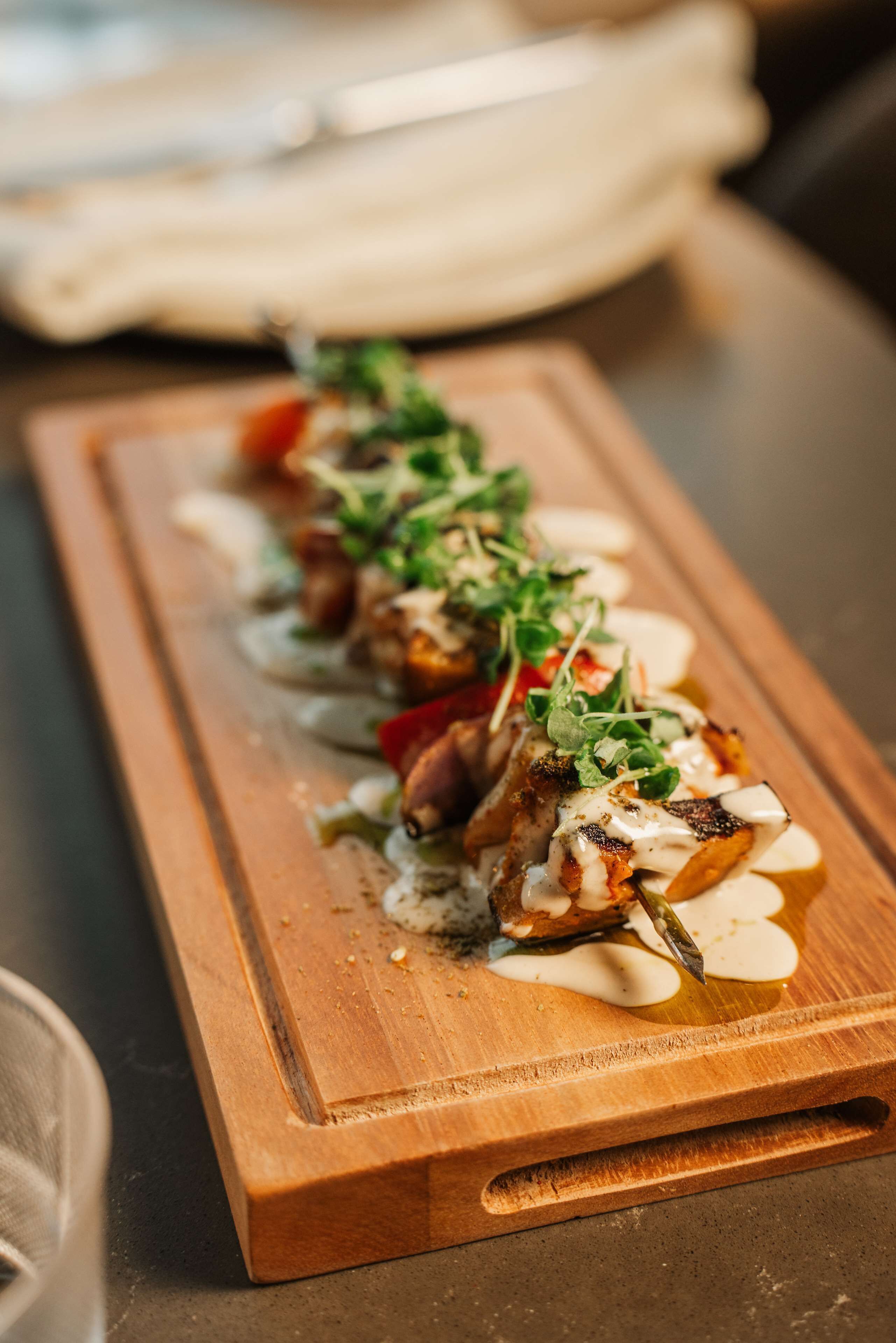A wooden serving board with a dish of food garnished with greens and sauce.