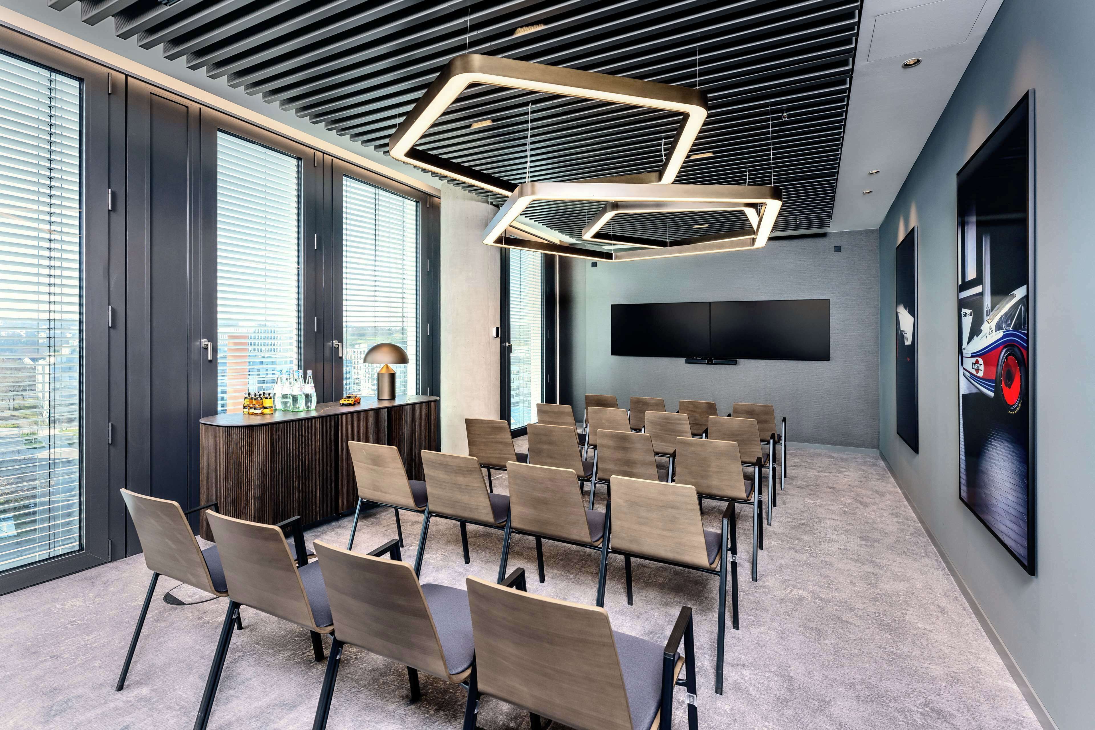 Une salle de conférence au design moderne, dotée d’une longue table entourée de chaises, d’un grand écran et d’un luminaire au plafond au design original.