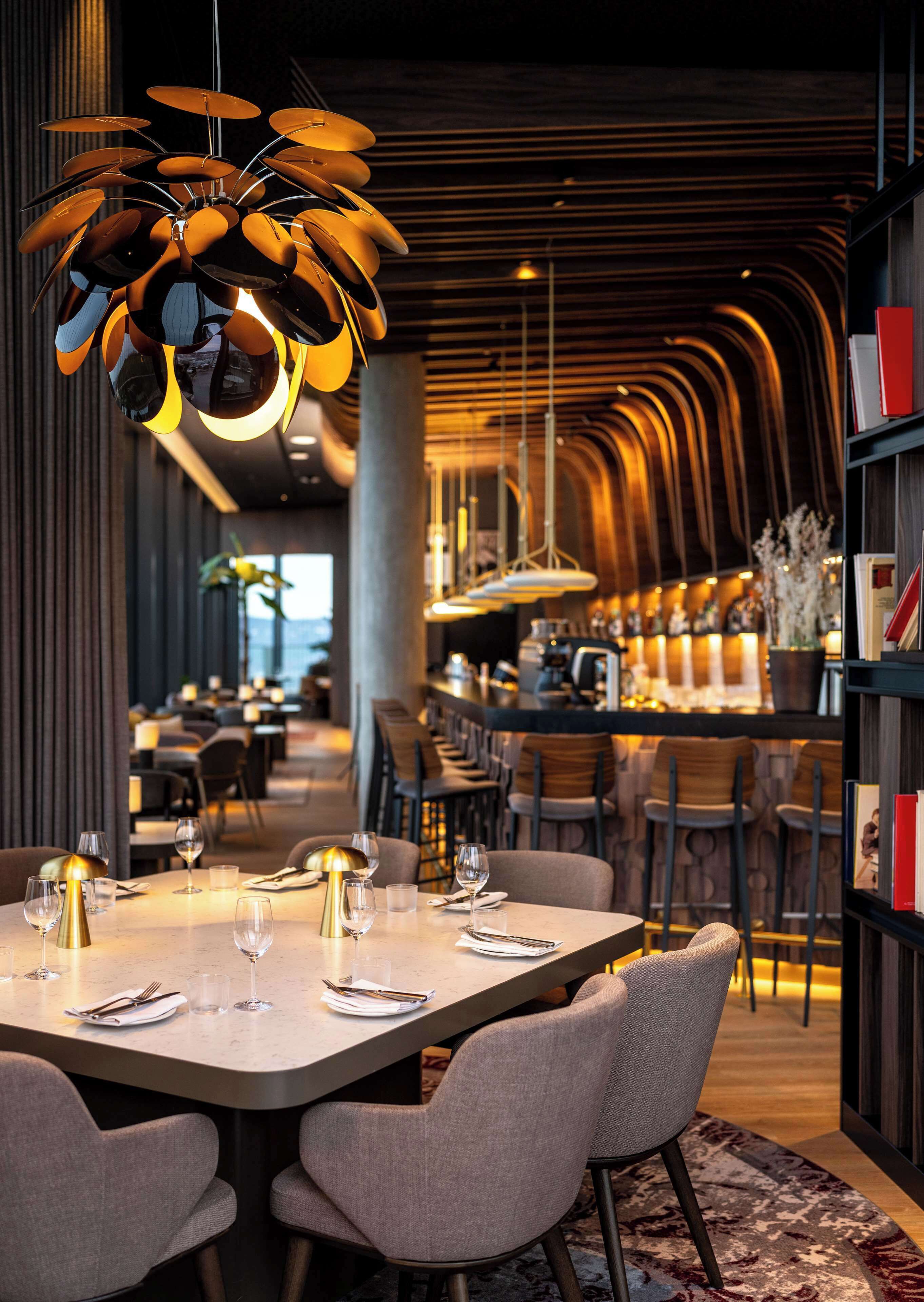 Ein modernes Restaurant mit langer Essbereich, hoher Decke und zeitgenössischen Leuchten.