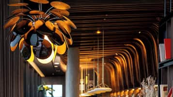 A modern restaurant interior with a long dining area, high ceiling, and contemporary lighting fixtures.