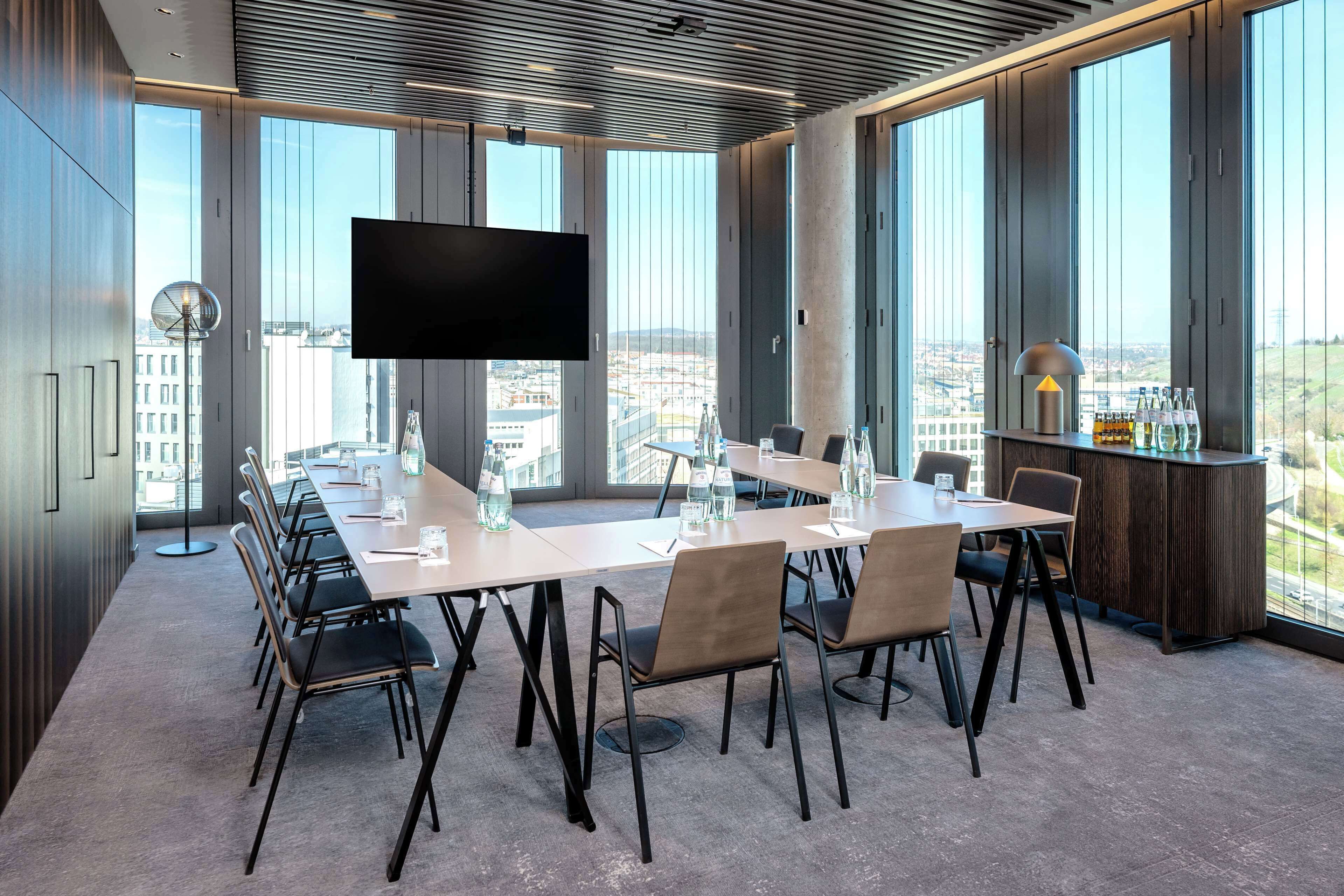 Ein Konferenzraum mit langem Tisch, Stühlen, einem Flachbildfernseher und großen Fenstern mit Blick auf die Stadt.