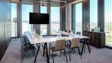 Ein Konferenzraum mit langem Tisch, Stühlen, einem Flachbildfernseher und großen Fenstern mit Blick auf die Stadt.
