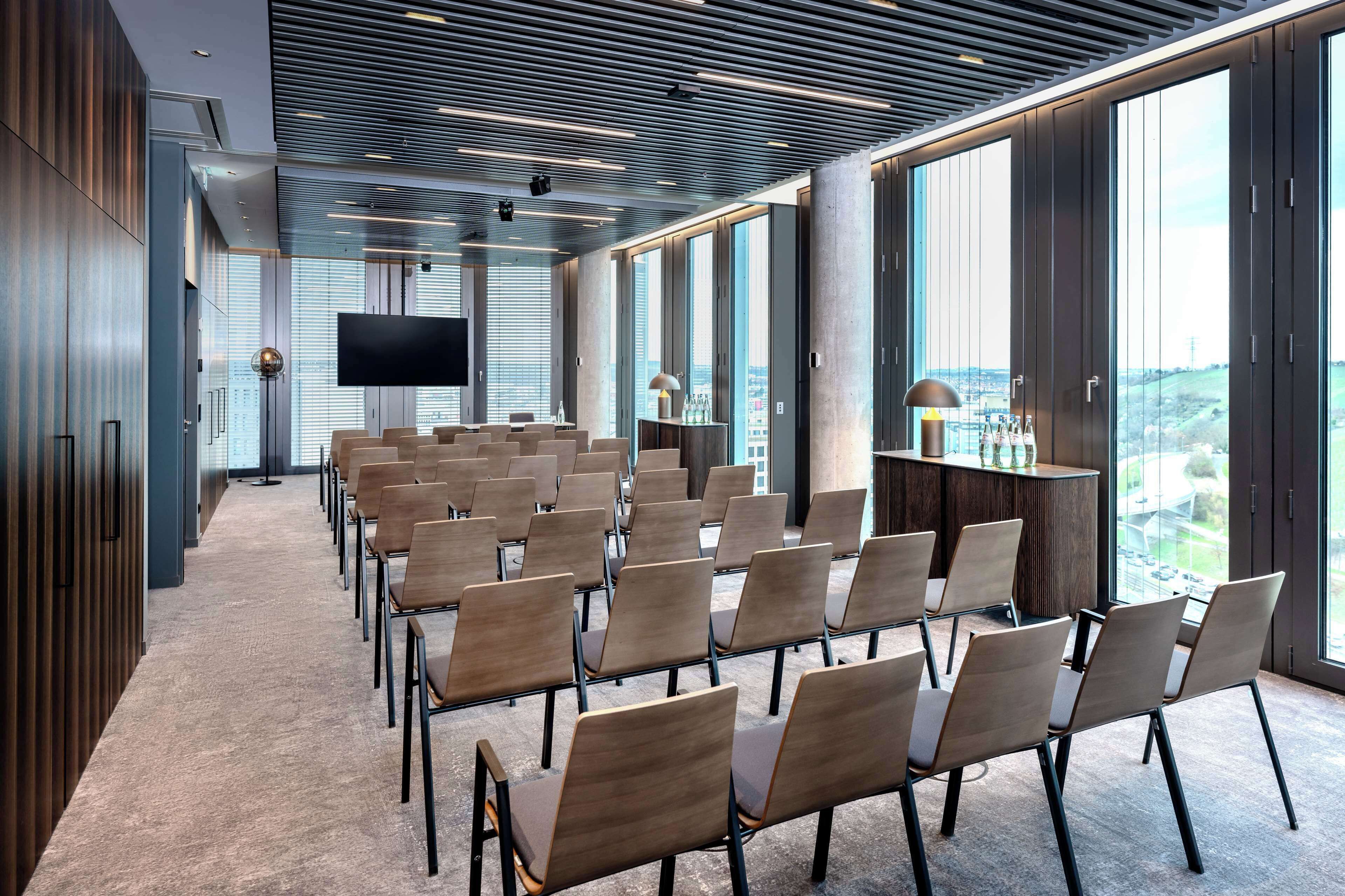 Una sala conferenze con file di sedie, un grande schermo piatto e vista sulla città attraverso ampie finestre.