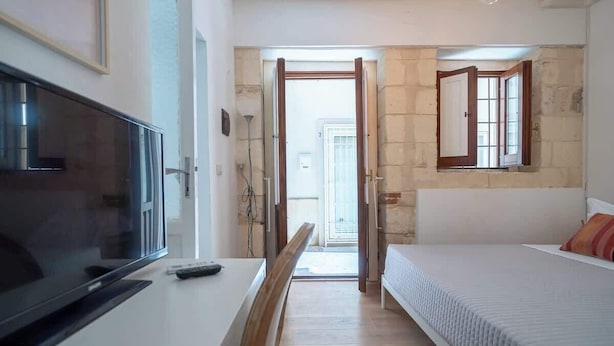 Une chambre avec un lit, une télévision et un bureau. Une porte donne sur un balcon.