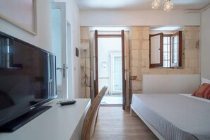 Un dormitorio con cama, televisor y escritorio. Una puerta da a un balcón.