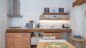 Une cuisine compacte dotée d’un plan de travail en bois, d’un four à micro-ondes, d’une cuisinière à gaz et d’un petit meuble blanc.