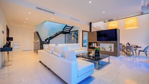 A modern living room with a white sofa, a glass coffee table, and a staircase leading to an upper level. - Villa Martin Stone Las Colinas Golf Country Club (VC)