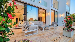 A modern outdoor living area with a sofa and chairs, a wooden deck, and potted plants. - Villa Martin Stone Las Colinas Golf Country Club (VC)