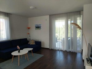 A living room with a dark blue sofa, a small round table, and a potted plant. - Vitorlás apartman 1 (Balatonszárszó)