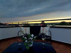 A rooftop terrace with two chairs, a table, and two wine glasses.