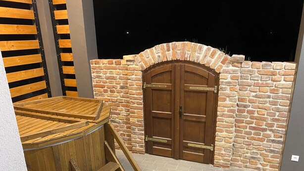 Een houten jacuzzi met een trap, een bakstenen muur en een houten deur.