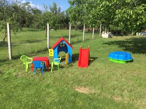 A fenced outdoor play area with a blue and red playhouse, a red slide, and a green and blue play structure.