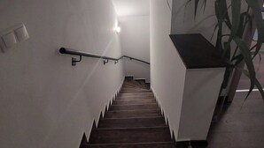 Een moderne trap met houten treden en een metalen leuning, die uitkomt op een plateau met een plafondlamp.