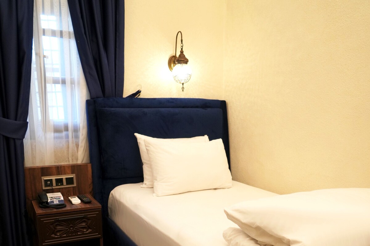 Habitació d'hotel amb un llit ben tendrà, una taula de nit amb una làmpada i una catifes amb disseny.