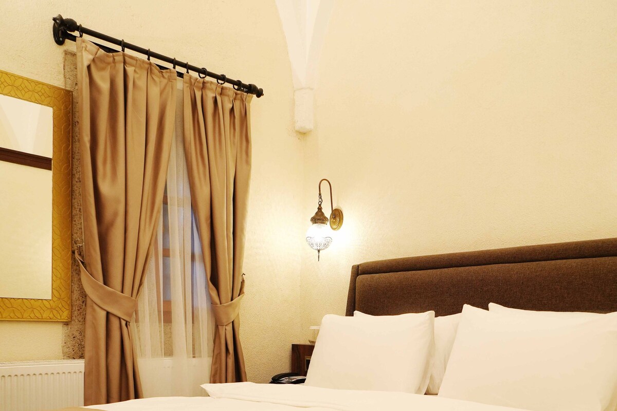 A neatly made bed with white linens, a brown headboard, and a window with beige curtains.