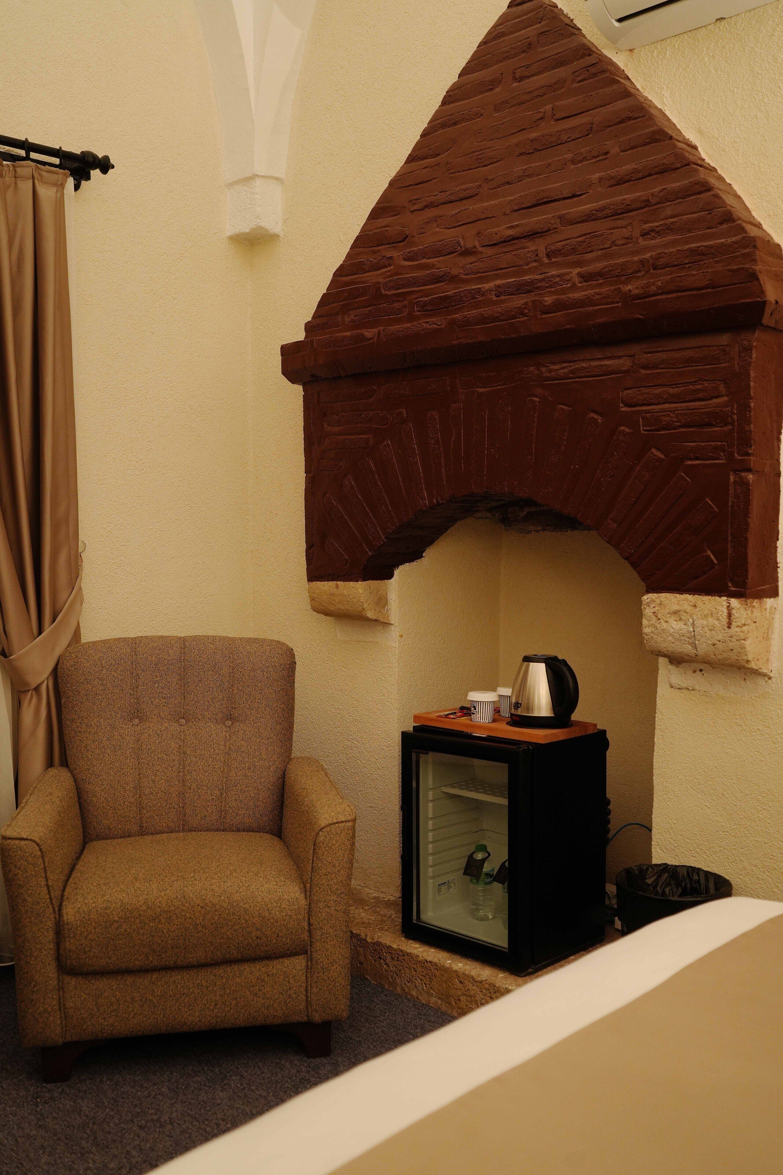 A room with a brick fireplace, a brown armchair, and a television on a stand.